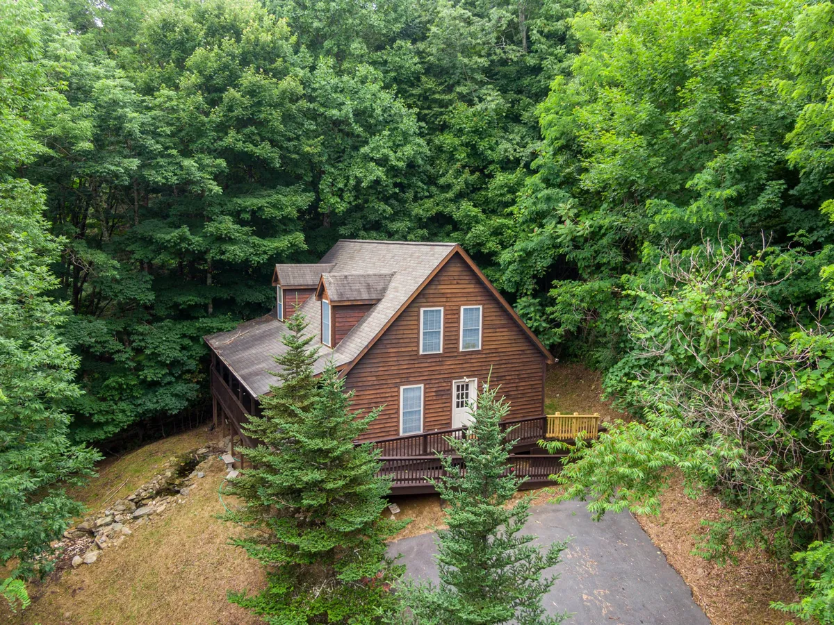 The hero image showcases a charming wooden cabin nestled among lush trees at 3,800 feet elevation, with a welcoming driveway leading up to the house. The scene is tranquil, with the cabin's porch inviting guests to relax and enjoy the natural beauty. The surrounding landscape promises peaceful mornings, starry nights, and opportunities for outdoor adventure.