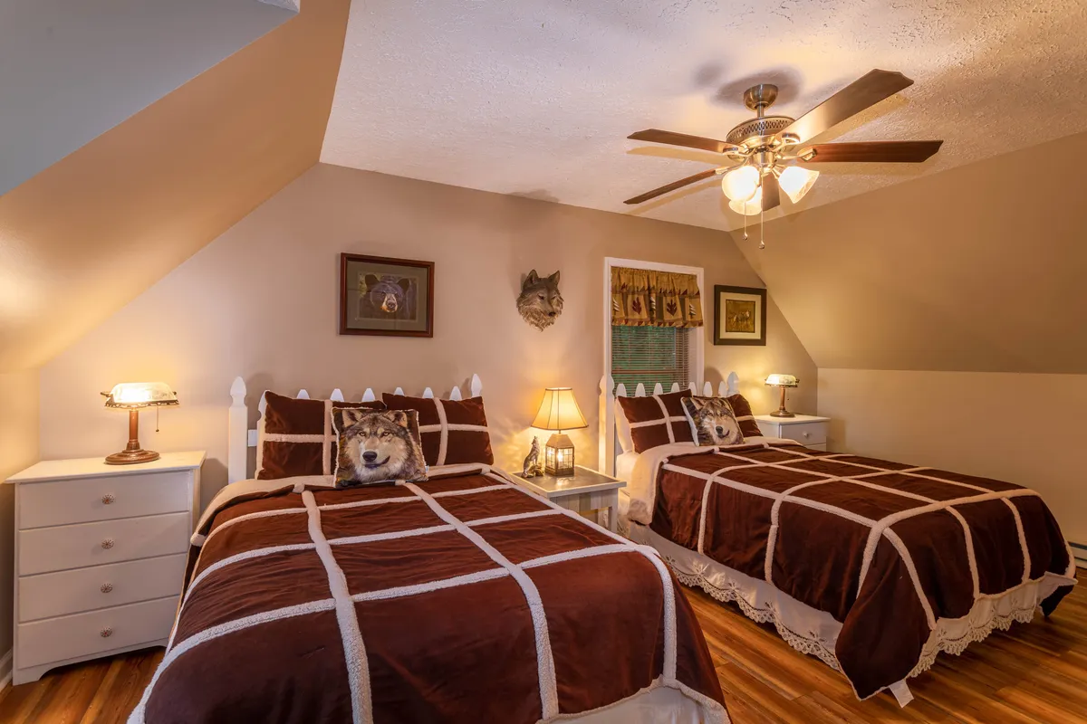 A bedroom with two beds dressed in brown patterned bedding, illuminated by warm table lamps. Wolf head decor and framed art lend a playful, family-friendly vibe—ideal for kids or groups.