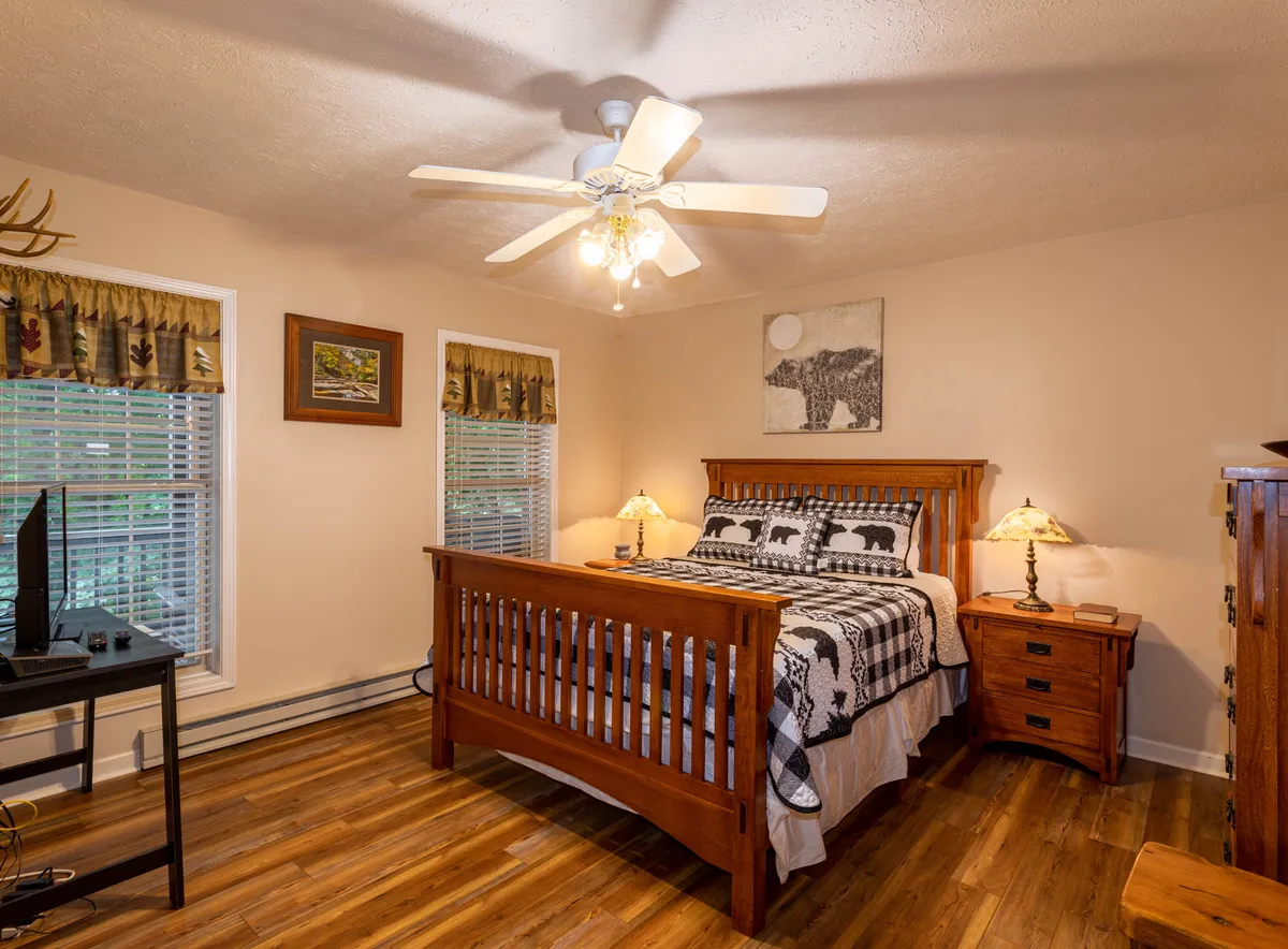 A cozy bedroom featuring a wooden bed frame with bear-themed bedding and a nightstand with a lamp. Natural light flows in, and bear-themed wall art adds a playful, restful touch. The space feels serene and is ideal for unwinding after a day of adventure.