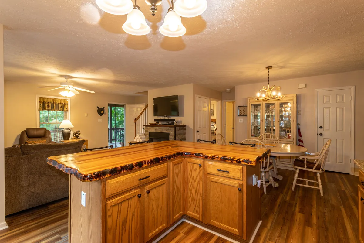 A panoramic interior shot encompassing the kitchen island, adjacent dining table, cozy sofa, and flat screen TV—all within one open, airy space. The setup invites both socializing and relaxation, with plenty of seating and surfaces for meals or entertainment.
