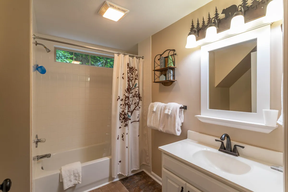 A calming bathroom space featuring a bathtub with a decorative shower curtain, sink with mirror, and shelf with decor items. The ambiance is serene and perfect for unwinding.