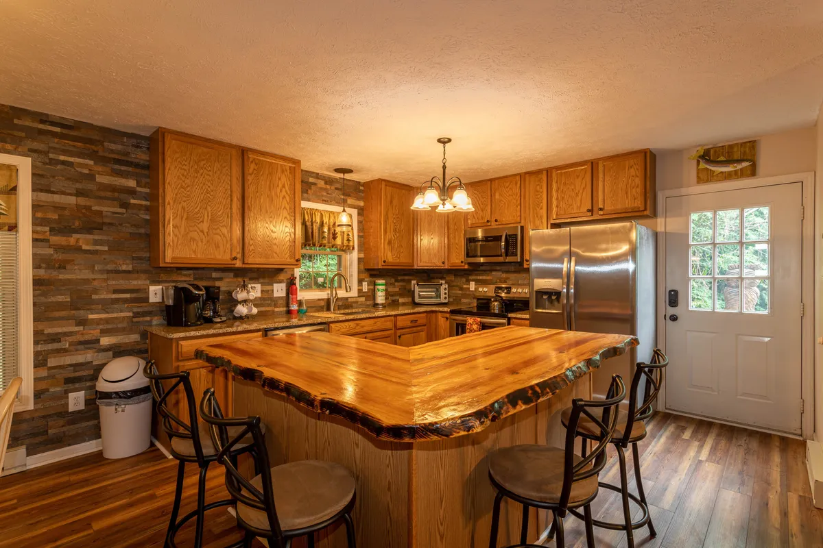 A closer look at the recently renovated kitchen, featuring a wooden countertop with bar stools, gleaming stainless steel appliances, and a textured stone wall, all contributing to a cozy yet modern vibe ideal for cooking and casual dining.
